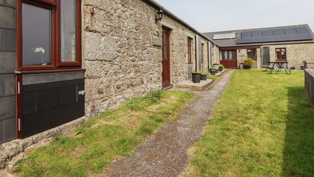 A stone building with multiple windows and doors, a gravel path, and a solar panel roof.