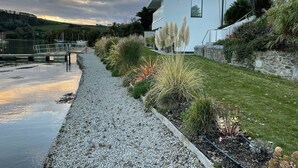 A modern building with a white exterior, a gravel pathway, and a grassy area with various plants.