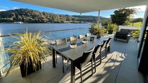 An outdoor patio with a table and chairs, potted plants, and a view of a lake and hills.