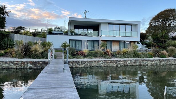 A modern two-story house with a wooden dock leading to a calm water body.