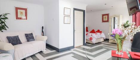 Una habitación de hotel moderna con un sofá, una cama con ropa de cama roja, un televisor y una mesa de vidrio con un florero.