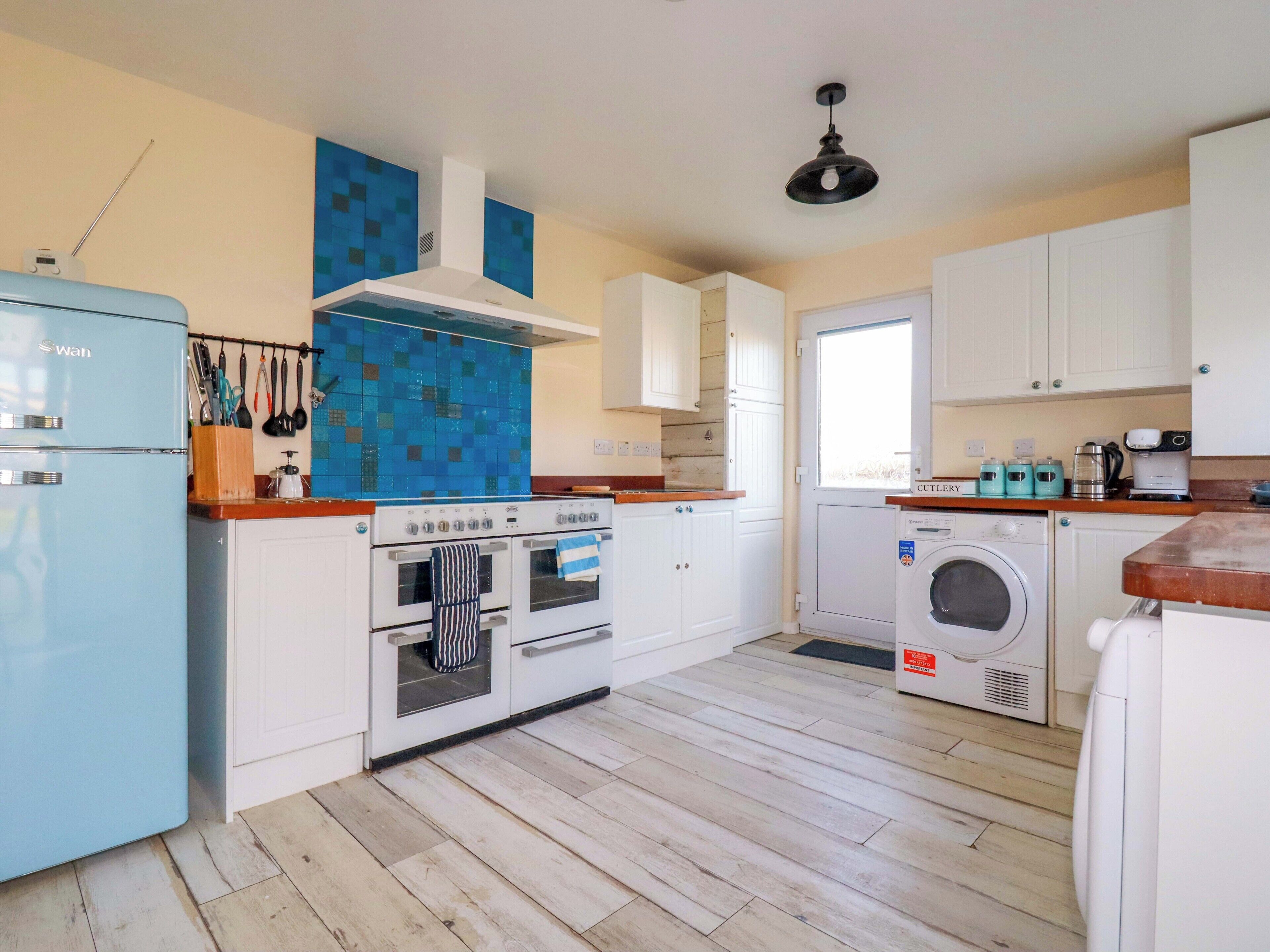A kitchen with a blue refrigerator, two ovens, a washing machine, and a window.