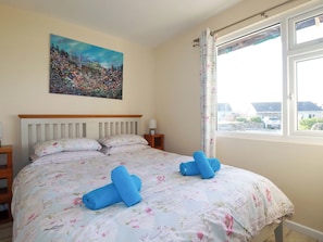 A bedroom with a bed, a painting on the wall, and a window with curtains.