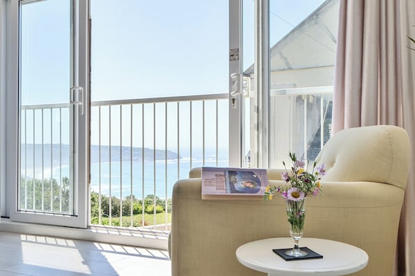 A room with a balcony, a chair, a small table with a vase of flowers, and a magazine. - Brook House (Penzance)