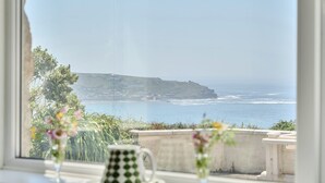 A coastal view from a window, including a cliff, sea, and a building in the distance. - Brook House (Penzance)
