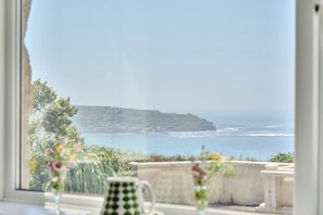 A coastal view from a window, including a cliff, sea, and a building in the distance. - Brook House (Penzance)