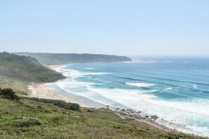 Un paysage côtier avec une plage, des vagues et un relief vallonné.