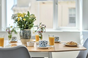 Une table de petit-déjeuner avec un vase de fleurs, un verre de jus d’orange, une tasse, une assiette avec un croissant et un bol de céréales.
