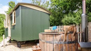 A green metal shed with a wooden door, a wooden barrel, and a metal grill.