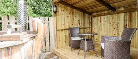 An outdoor patio with a wooden deck, two wicker chairs, a small table, and a metal barbecue grill.