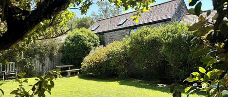 A stone house with a sloped roof, surrounded by a well-maintained lawn and dense shrubbery.