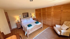 A bedroom with a wooden bed, bedside tables with lamps, a wooden wardrobe, a sofa, and a rug.