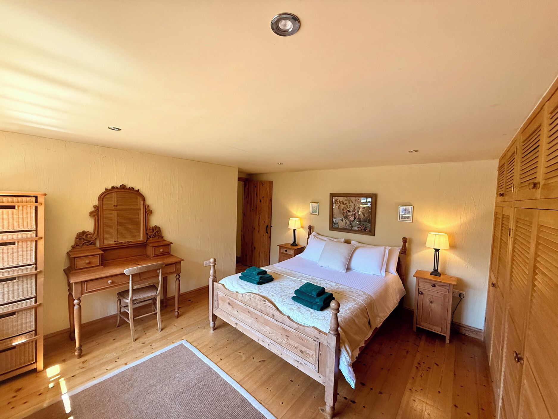 Quarto com cama de madeira, mesas de cabeceira, escrivaninha, cadeira e guarda-roupa.
