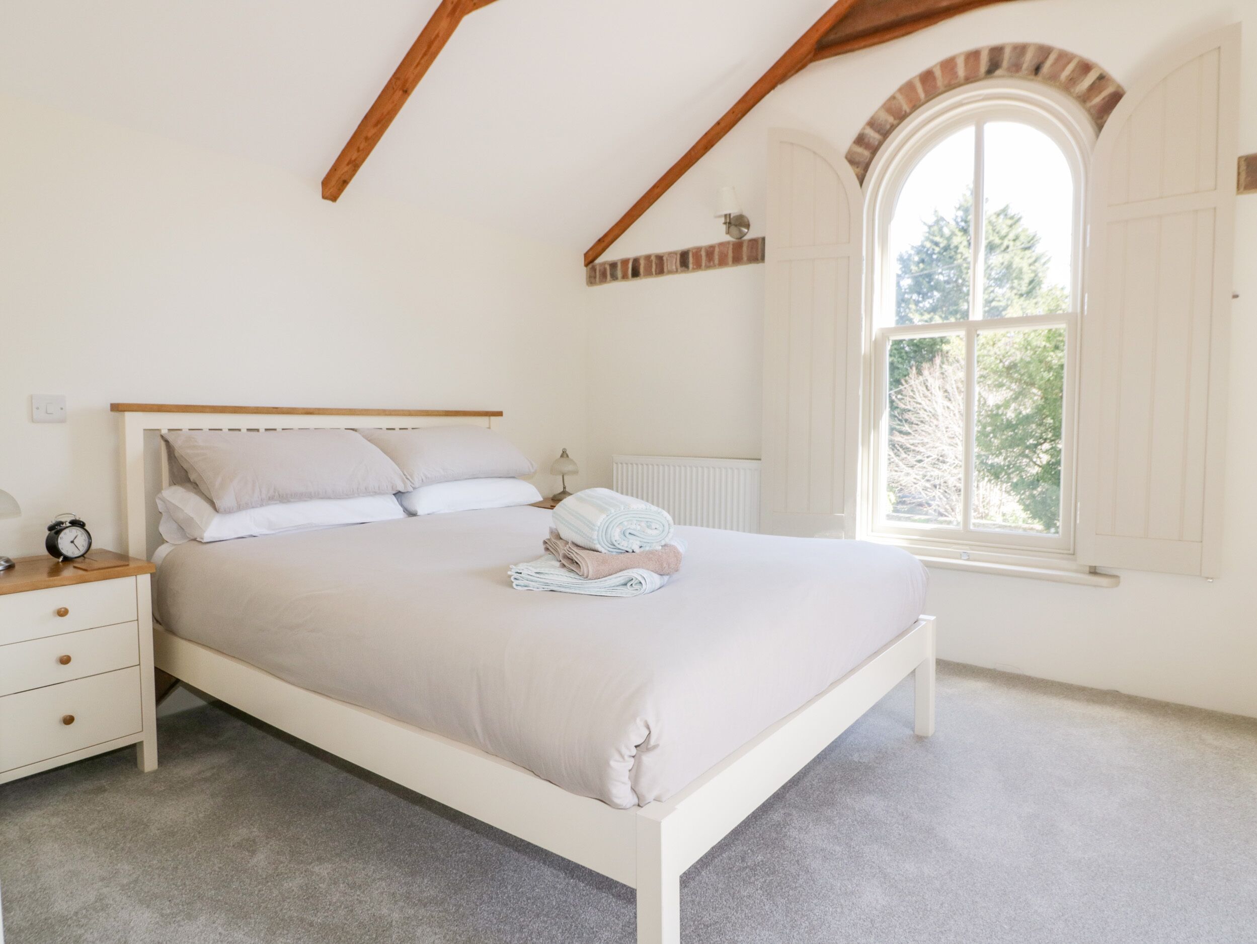 Un dormitorio con una cama, una mesita de noche, una lámpara, una ventana y un radiador.