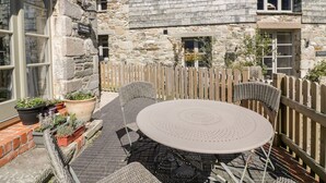 A stone building with a wooden fence, a round table with chairs, and potted plants. - The Old Smithy (St. Columb Major)