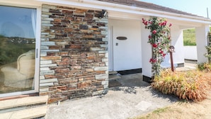 A house with a stone facade, a glass door, and a small porch with a flower planter. - The Shack (Newquay)