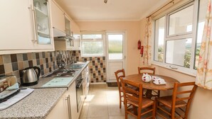 A kitchen with a dining table and chairs, a window with curtains, and a view of the outdoors. - The Shack (Newquay)