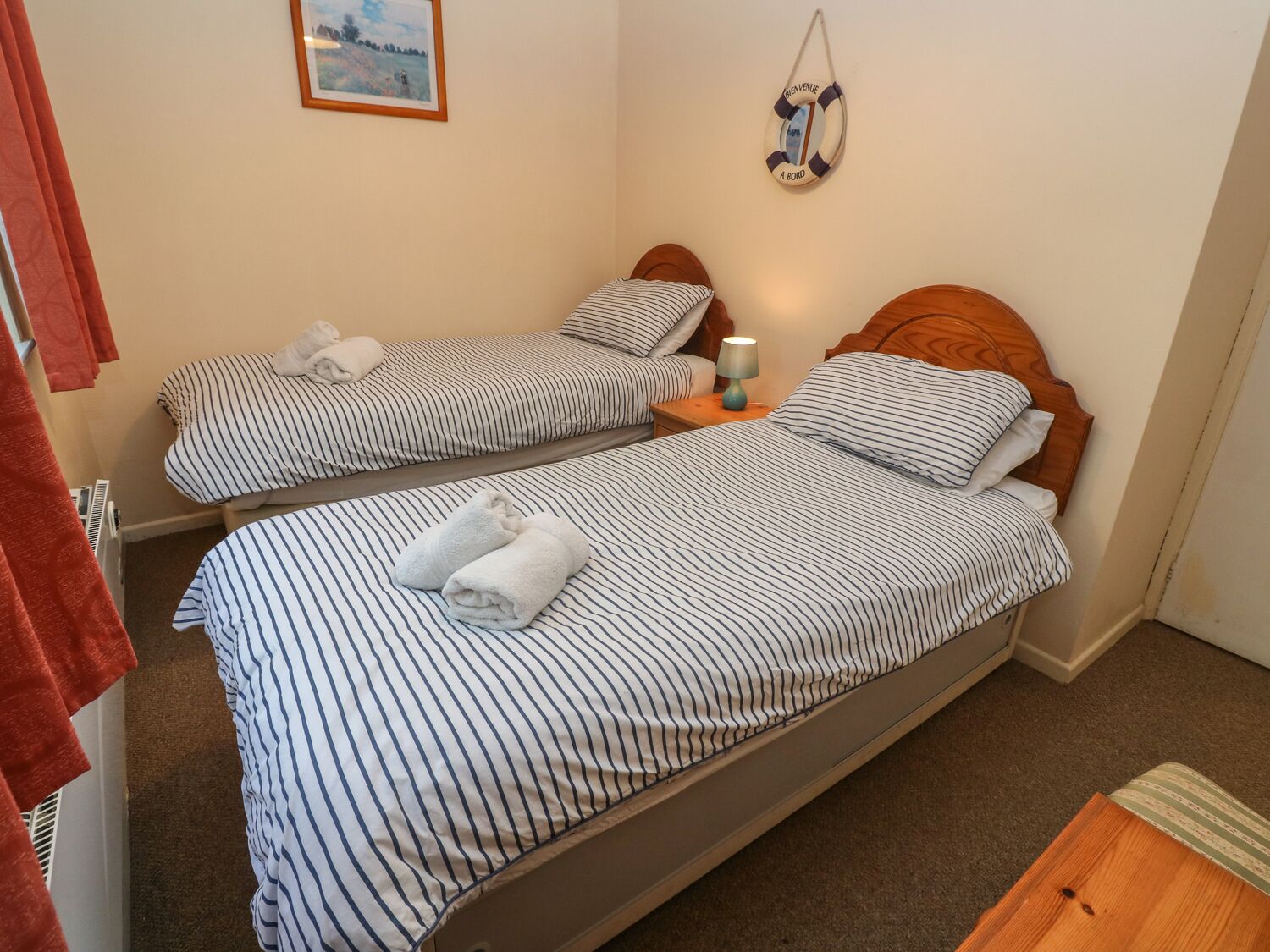A double bed with striped bedding, a bedside table with a lamp, and a wall-mounted life preserver decoration.