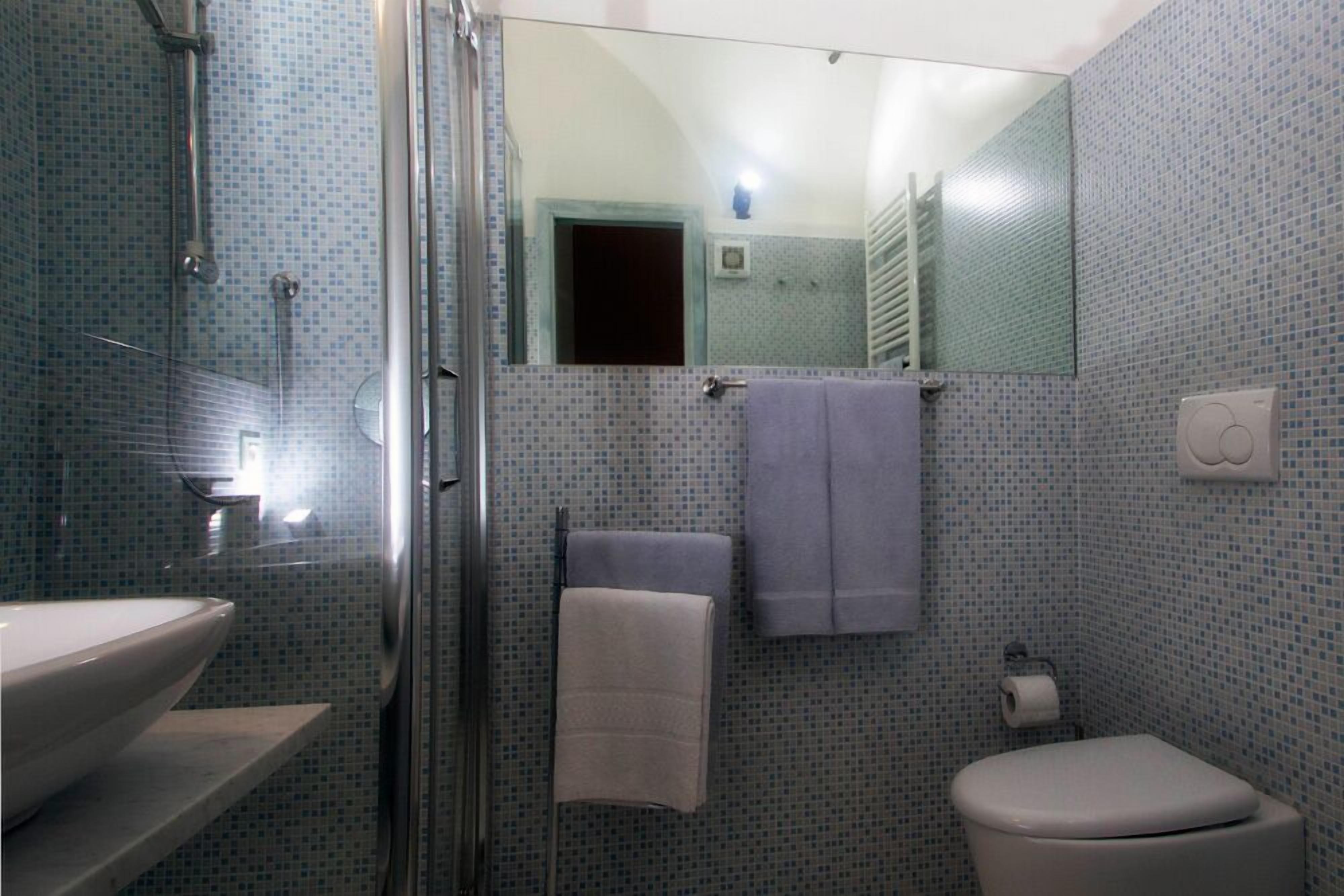 A bathroom with a glass shower enclosure, a sink, a toilet, and a mirror.