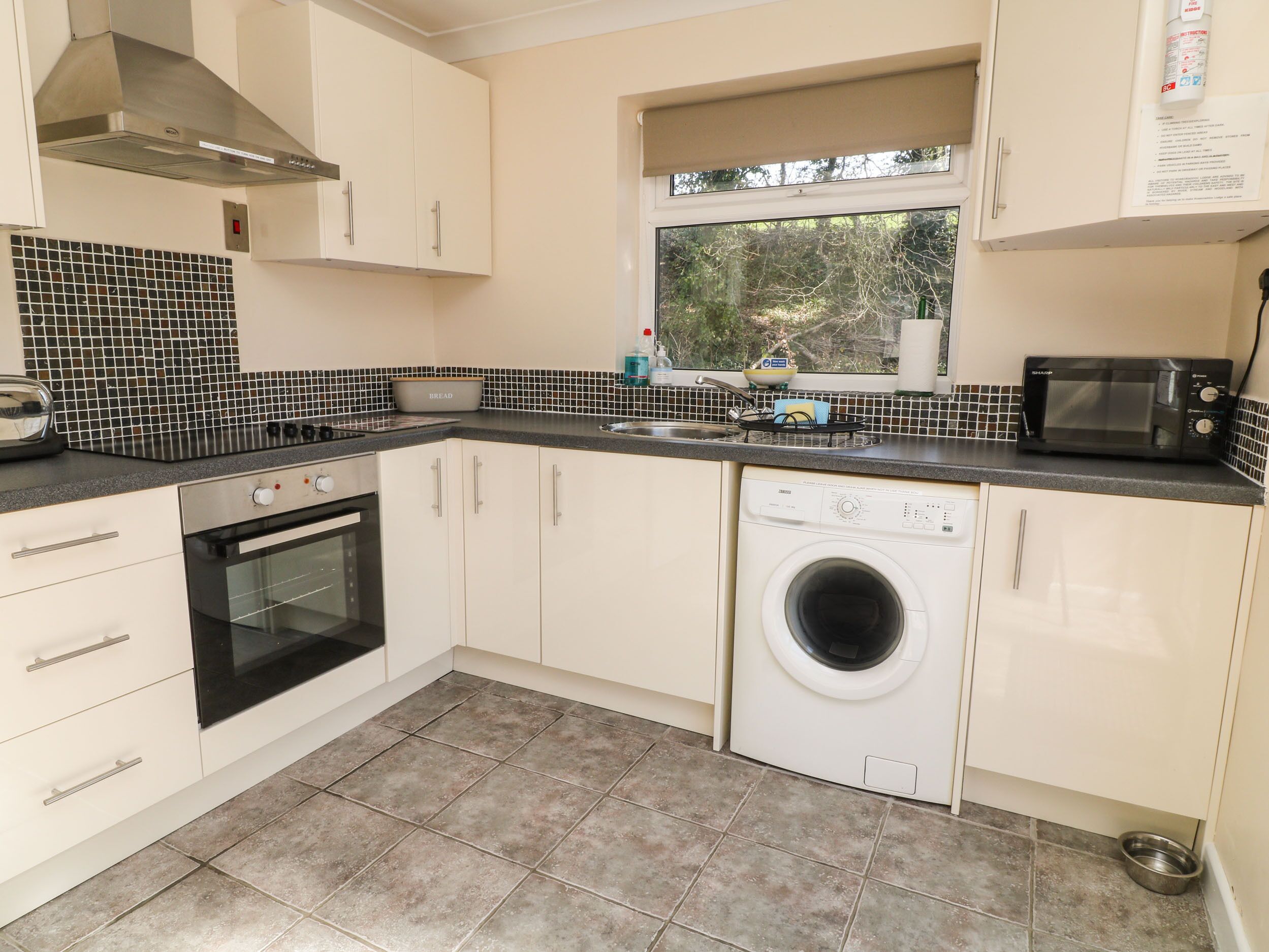 A compact kitchen with white cabinets, a built-in oven, a washing machine, and a microwave.