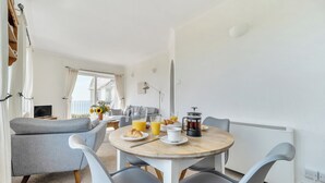 Une pièce moderne et bien éclairée, avec une table de salle à manger ronde, des chaises à revêtement gris, une machine à café et des produits pour le petit-déjeuner.