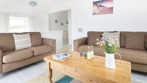 A modern living room with two sofas, a wooden coffee table, and a potted plant. - The Coach House (Penzance)