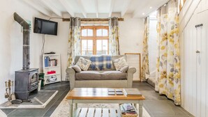 A cozy living room with a sofa, a wooden table, a television, a fireplace, and a bookshelf. - Victoria Cottage (Newquay)