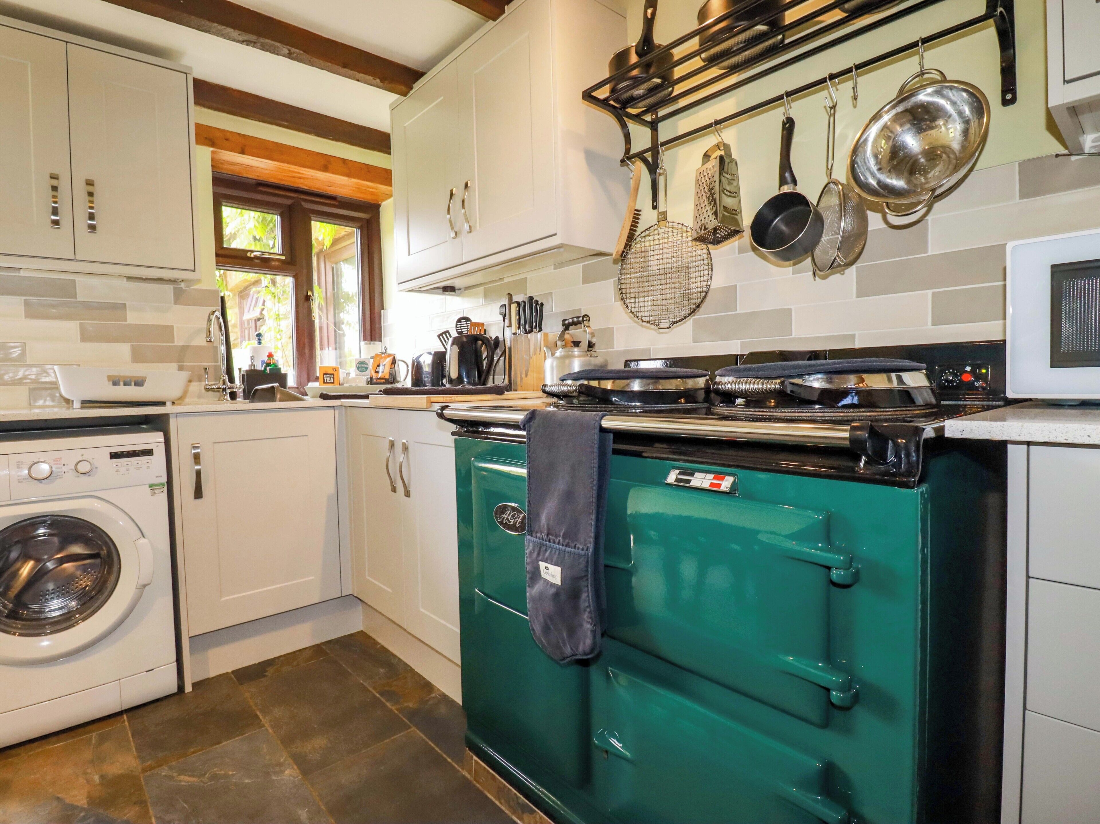 A kitchen with white cabinets, a green stove, a washing machine, and a hanging pot rack.