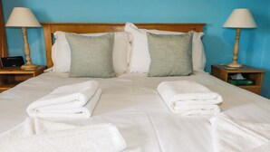 A neatly made bed with white linens and green pillows, two bedside tables with lamps, and a blue wall.