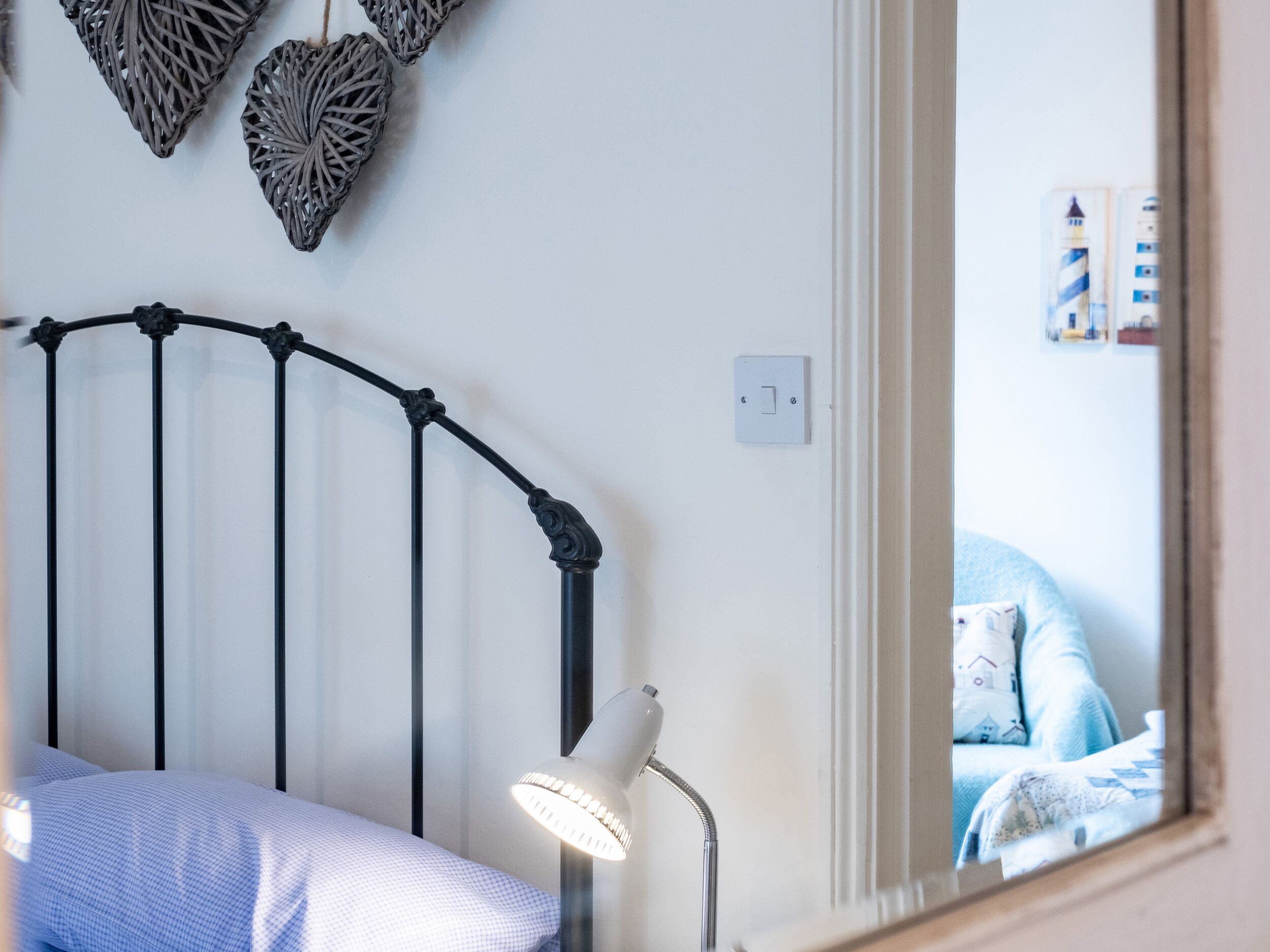 Un dormitorio con una cama, una lámpara de noche y un espejo que refleja una cama con un edredón estampado.