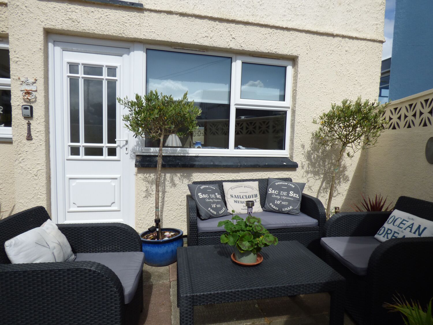A patio area with wicker furniture, a small table with a plant, and a window with two potted plants.