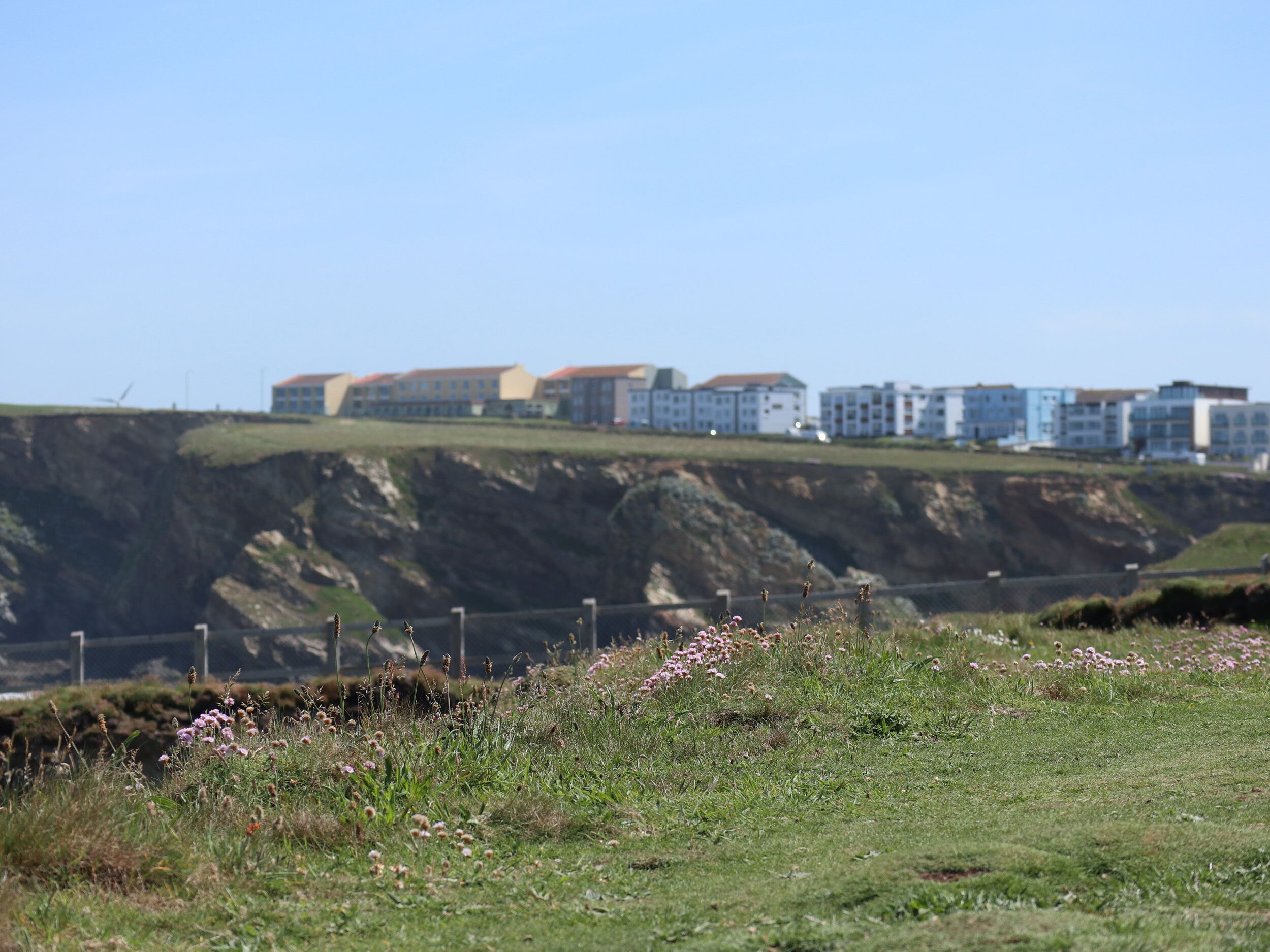 A coastal landscape with a cliff and buildings in the background.