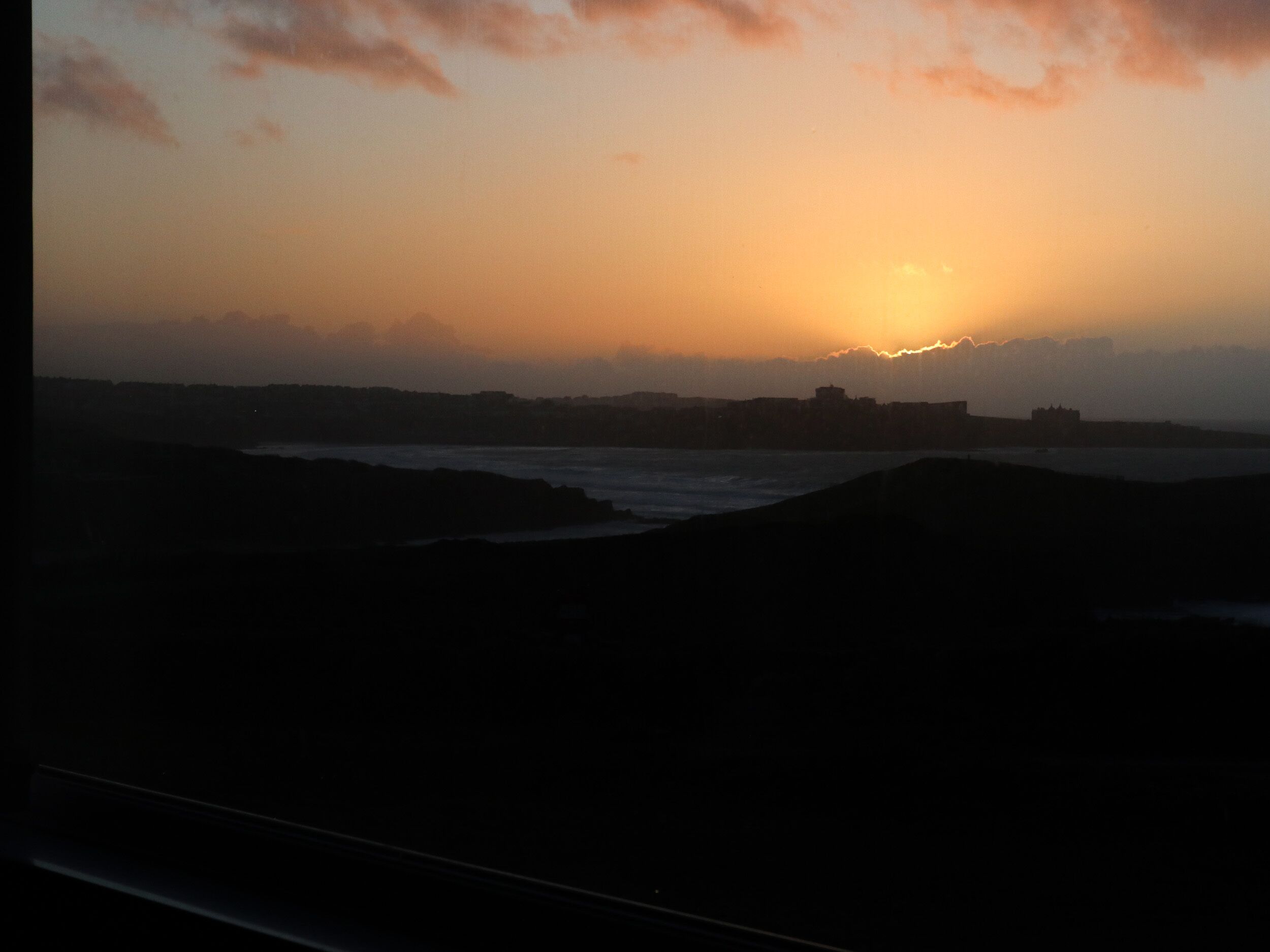 A sunset over a coastal landscape with buildings silhouetted against the sky.