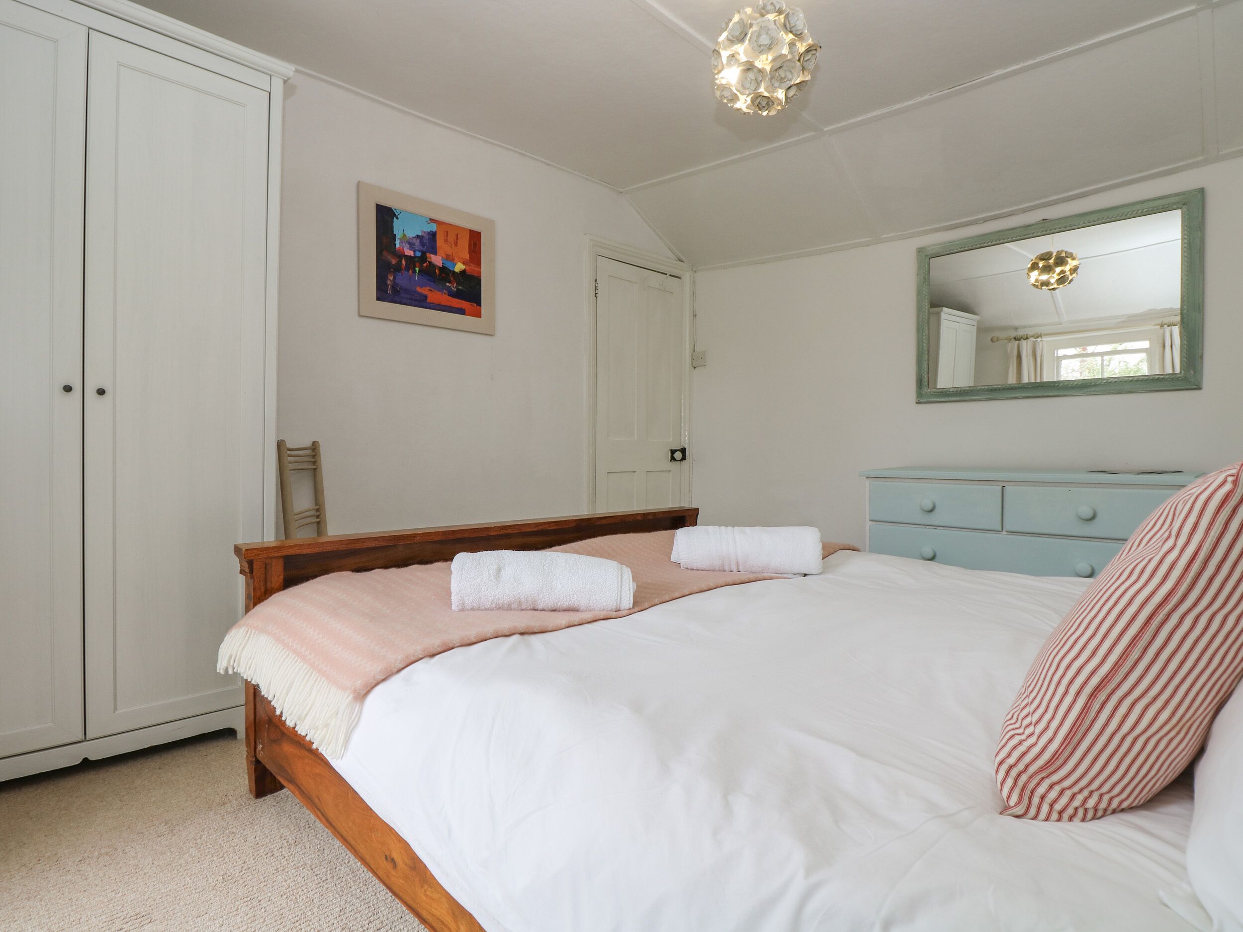 Quarto com uma cama grande, cabeceira de madeira, mesa de cabeceira, cômoda, espelho e uma porta.