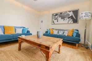 Un salon avec deux canapés bleus, une table basse en bois et un lampadaire.