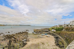 Une zone côtière où des bateaux sont amarrés près d’une côte rocheuse, avec un phare et des bâtiments situés sur une colline.