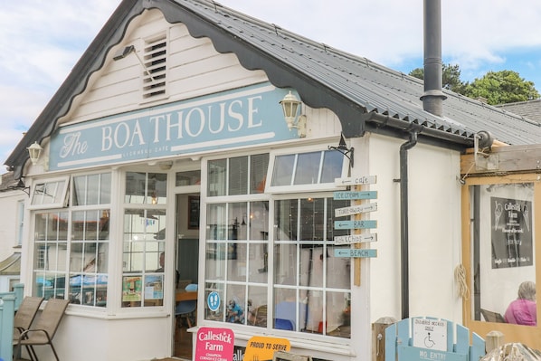 Un bâtiment portant l’inscription « THE BOATHOUSE », avec une enseigne indiquant « Café agréé » et divers panneaux indiquant la direction des différents services, comme un stand de glaces et un bar.