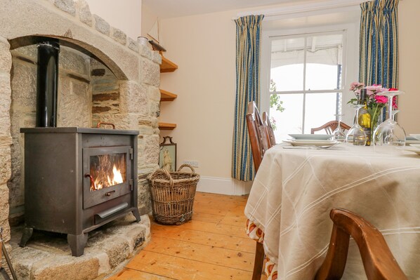 Une cheminée en pierre avec un feu apparent, une table à manger dressée avec des assiettes et des verres, et une fenêtre ornée de rideaux à rayures.