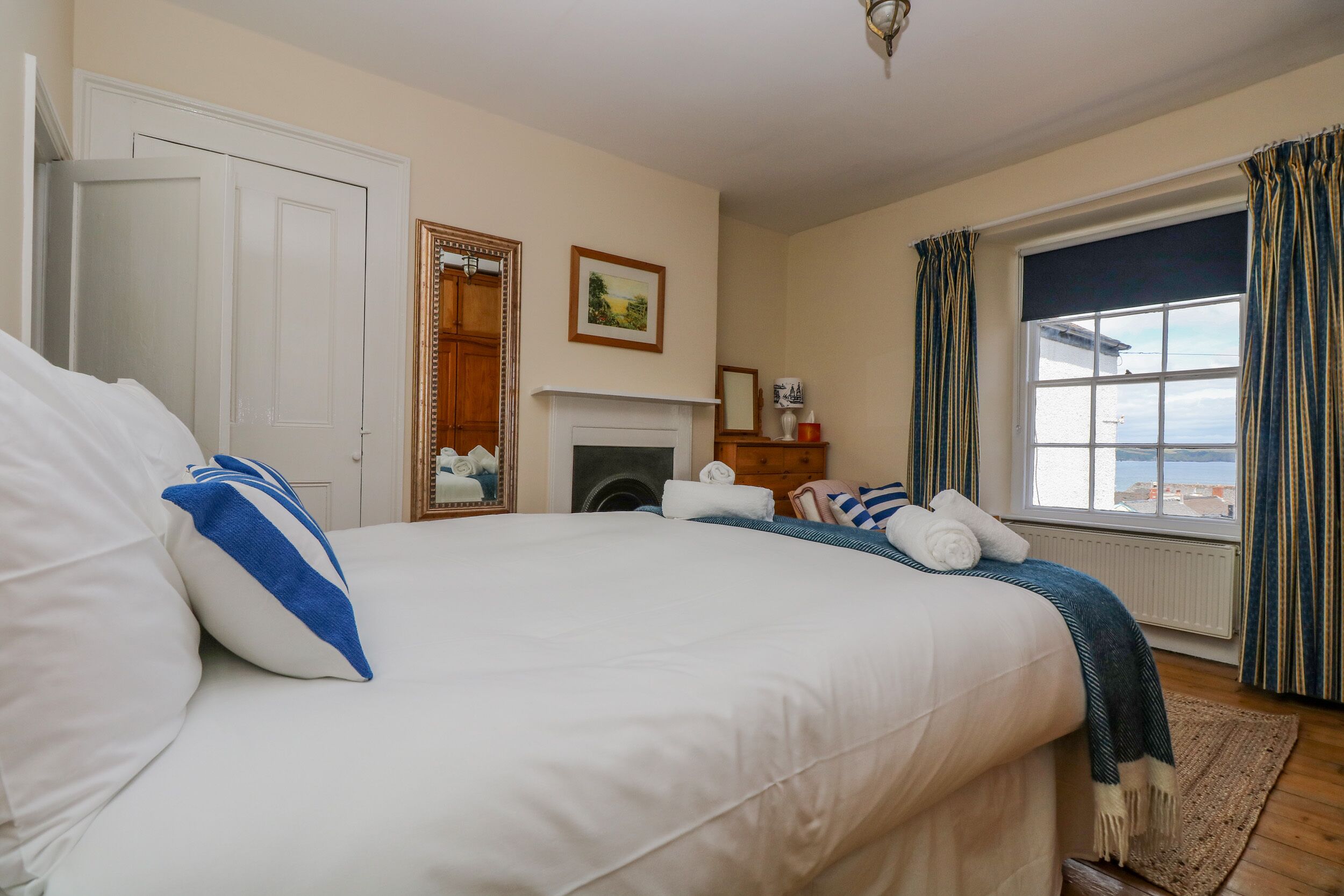 Une chambre à coucher avec un grand lit, une cheminée, une fenêtre avec des rideaux et une vue sur la mer.
