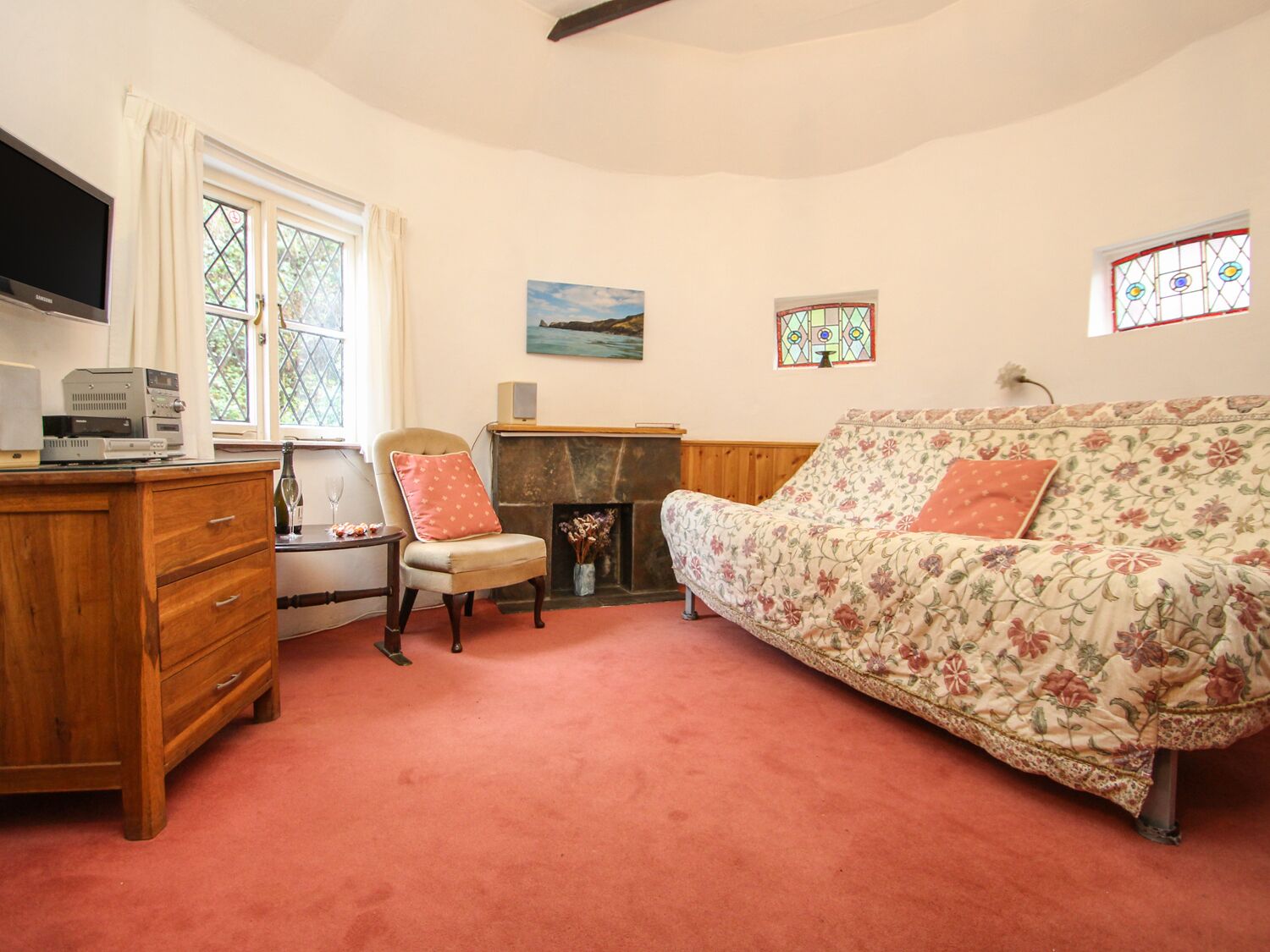 A cozy room with a wooden dresser, a floral sofa, a chair, a fireplace, and a television.