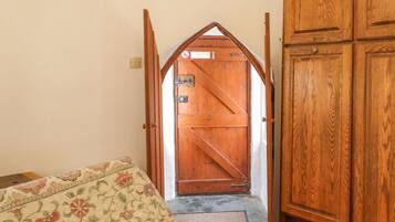 A room with a wooden door, a bed with a floral bedspread, and a wooden wardrobe.