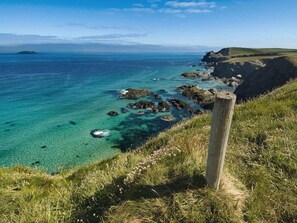 A coastal landscape with clear turquoise waters, rocky outcrops, and grassy terrain. - The Old Dairy (Wadebridge)