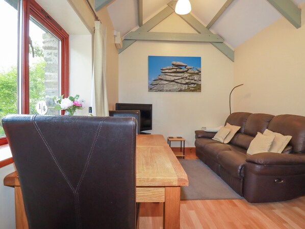 A cozy living room with a wooden table, a leather sofa, and a painting of rocks on the wall. - Barn Cottage (Liskeard)