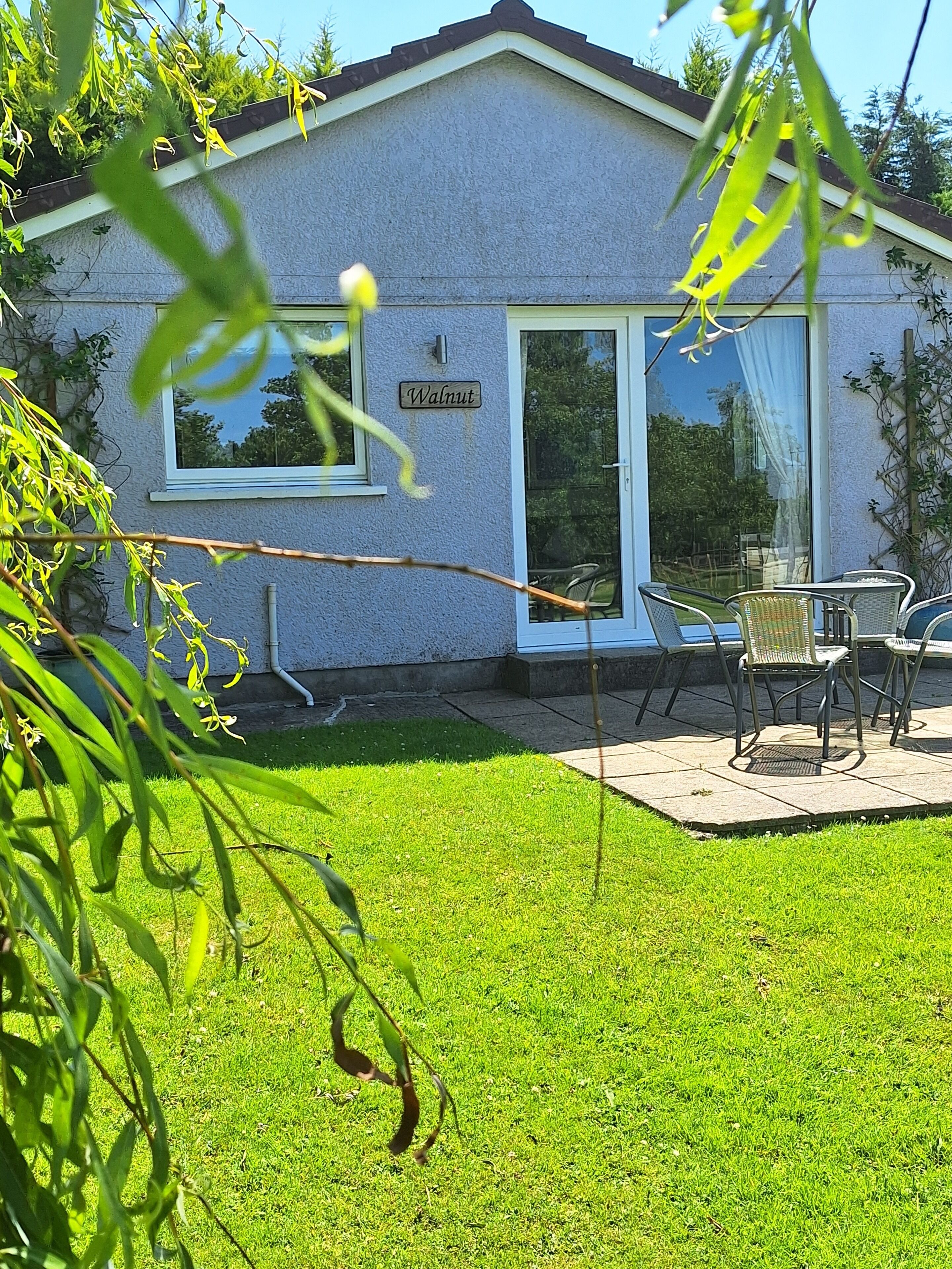 A house with a sign reading "Walnut" on the door, a patio with chairs, and a well-maintained lawn.