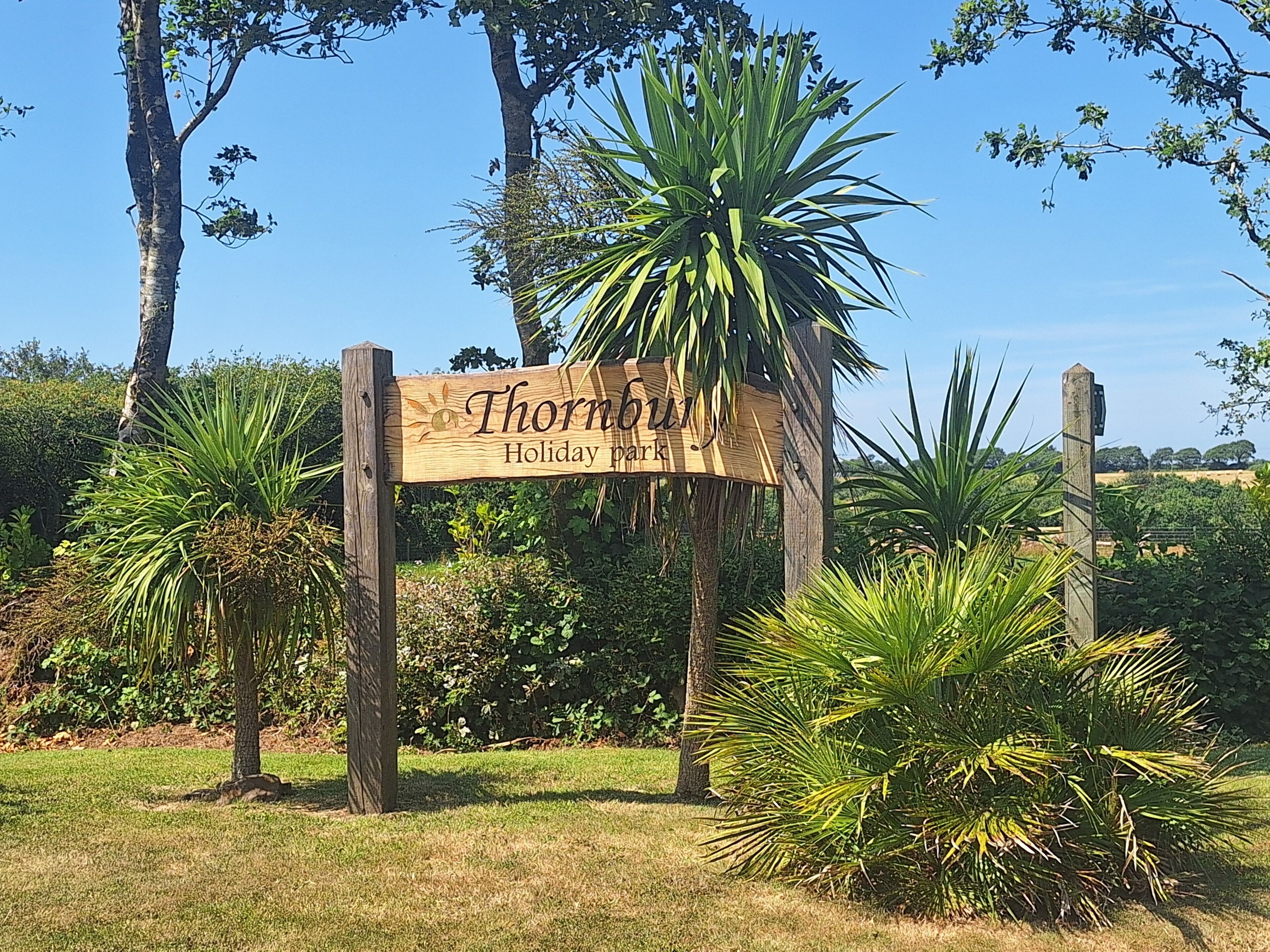 Un segnale di legno con la scritta 'Thornhill Holiday Park' circondato da vegetazione e alberi.