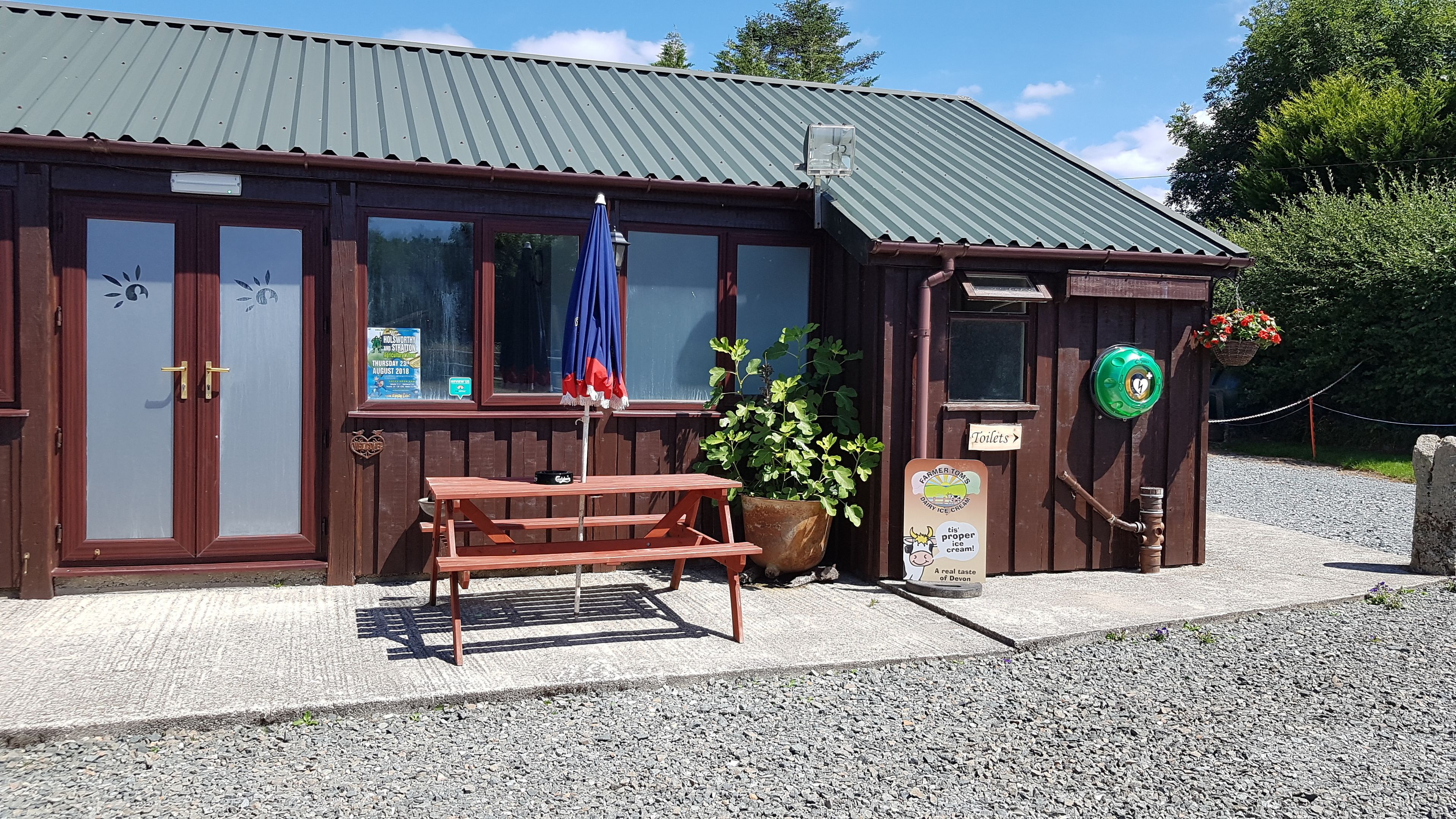 A wooden building with a green roof, a bench, a potted plant, and a sign indicating a toilet.