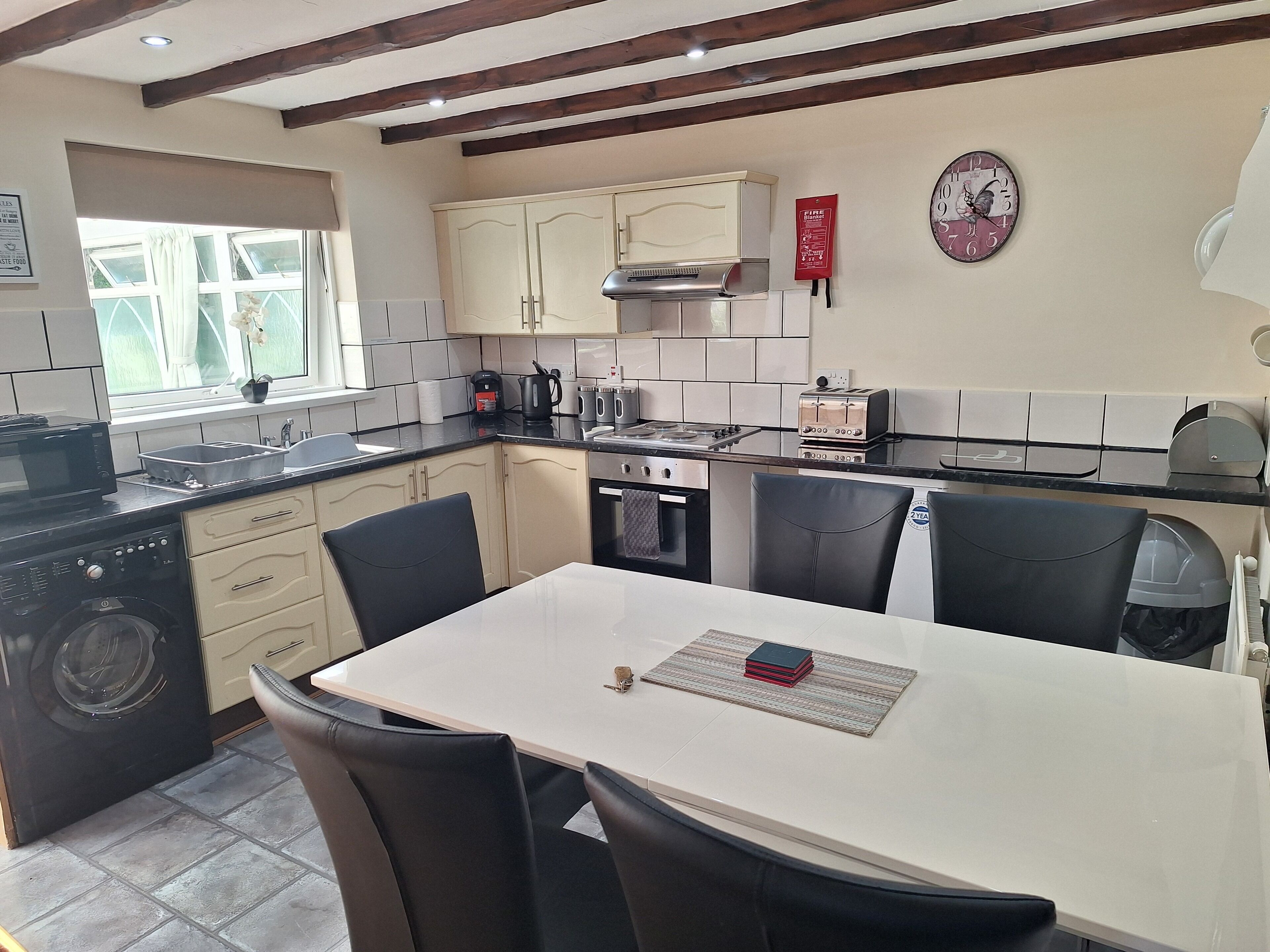 A kitchen with a dining table, chairs, a sink, a stove, and a window with curtains.