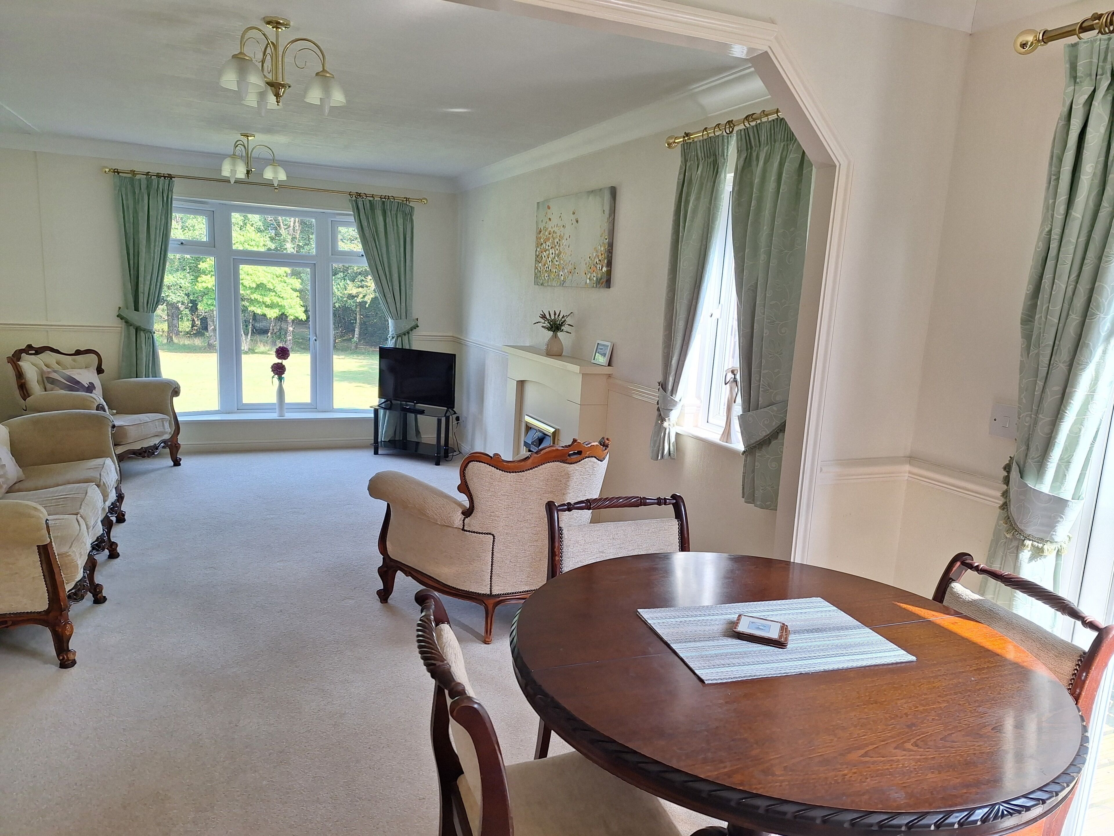 A room with a round wooden table, several upholstered chairs, a television, and a fireplace.