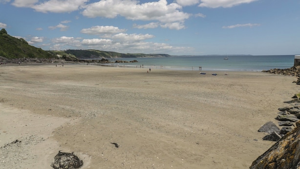 A wide sandy beach with a rocky shoreline, a clear blue sky, and distant hills. - Cosy Cottage (Liskeard)