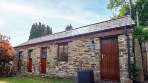 A stone cottage with a red door, a small window, and a sign indicating it is a guesthouse. - Cosy Cottage (Liskeard)